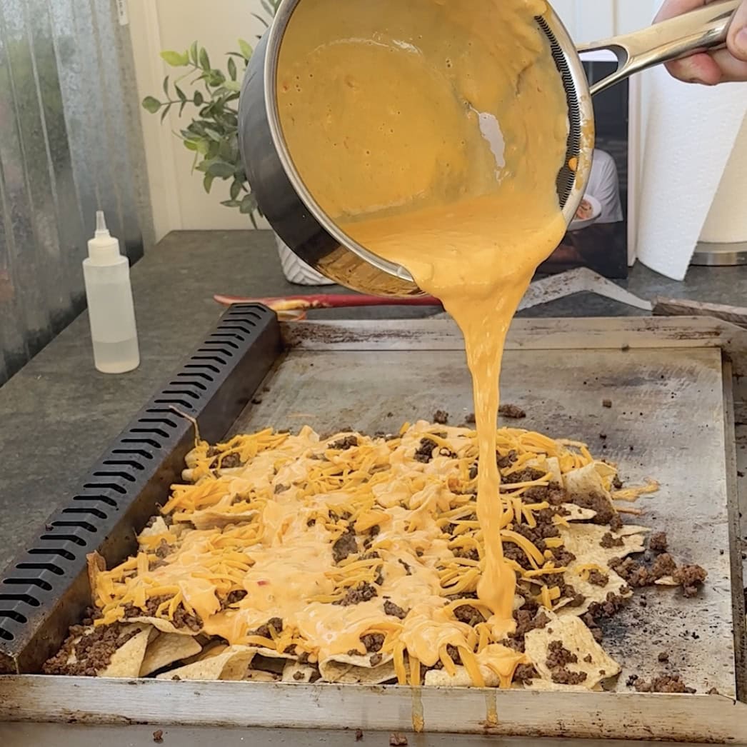 Nacho cheese being poured onto nachos on the griddle.