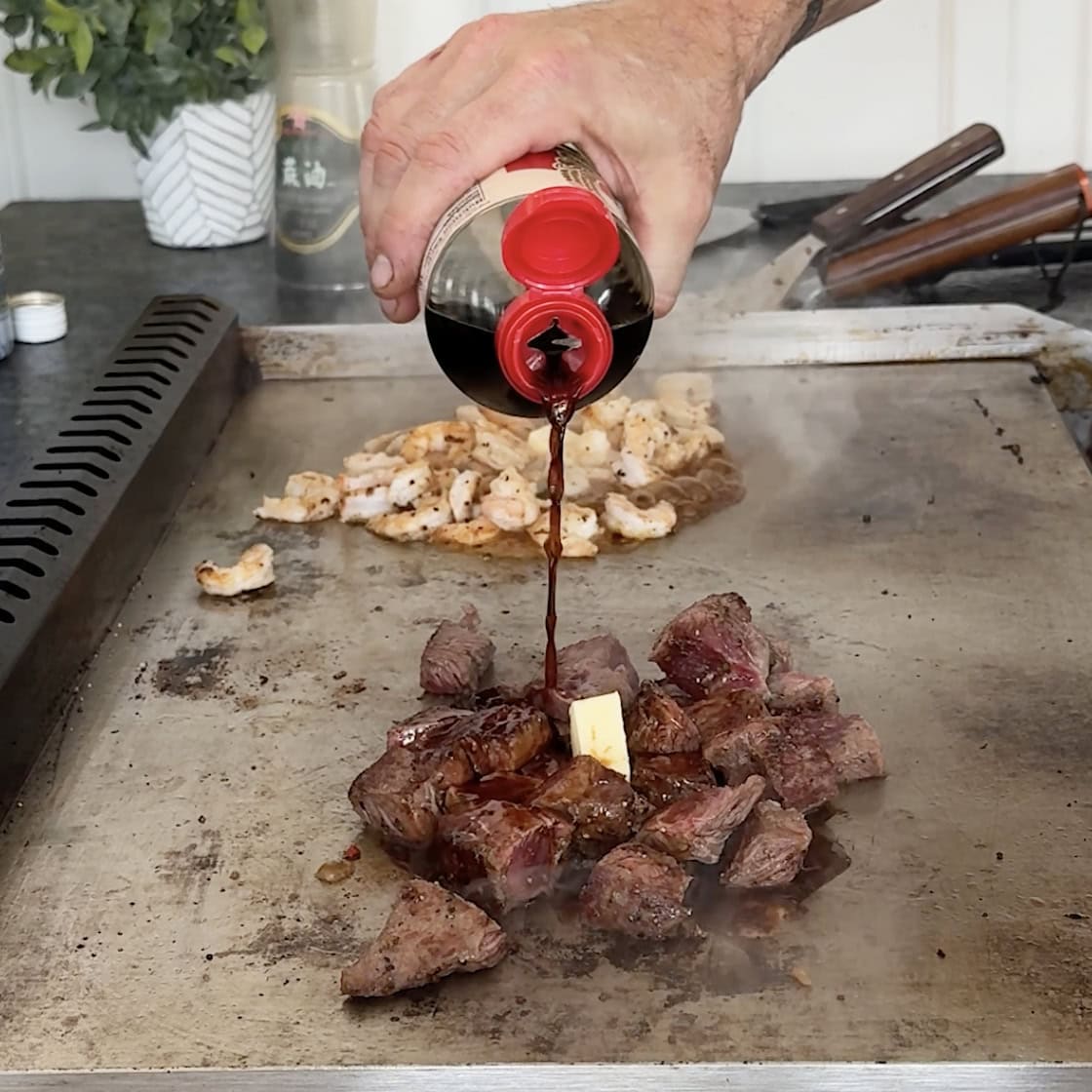 Cooking steak on the griddle and pouring Soy Sauce on top.