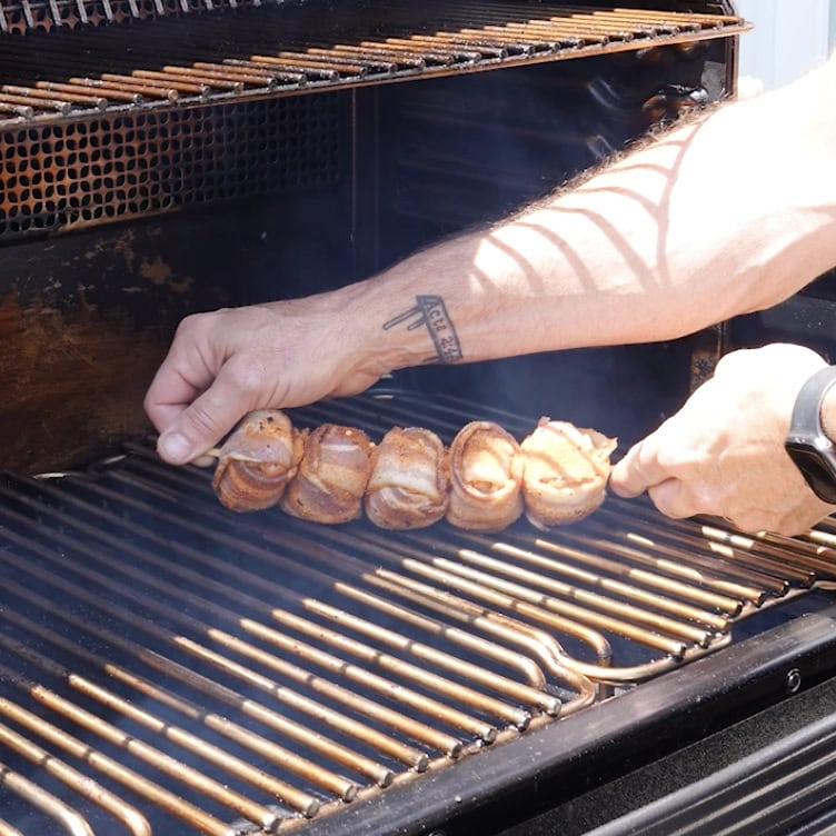 Placing the thighs wrapped in bacon onto the smoker.