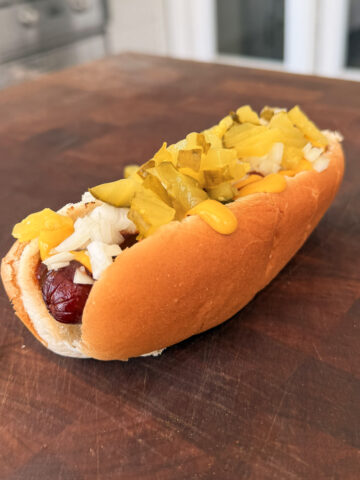 A hot dog topped with mustard and pickles.