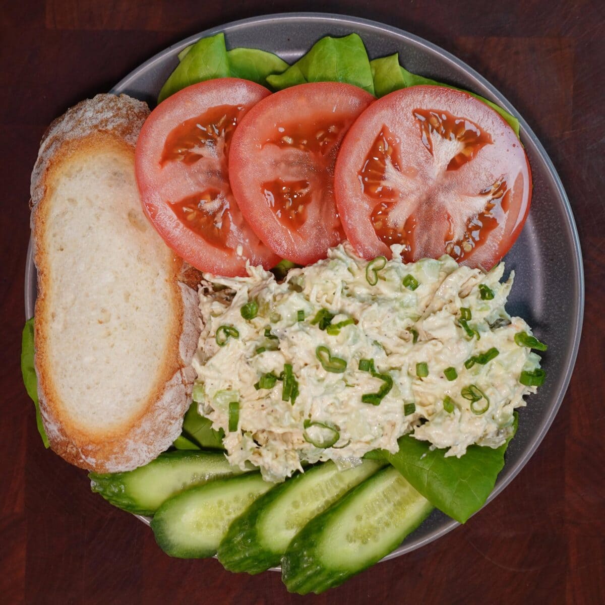 chicken salad on a plate with sourdough bread, cucumbers and tomatoes