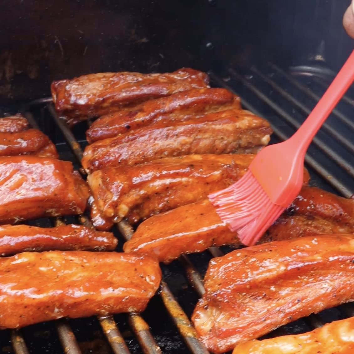 Brushing BBQ sauce onto ribs on the smoker.
