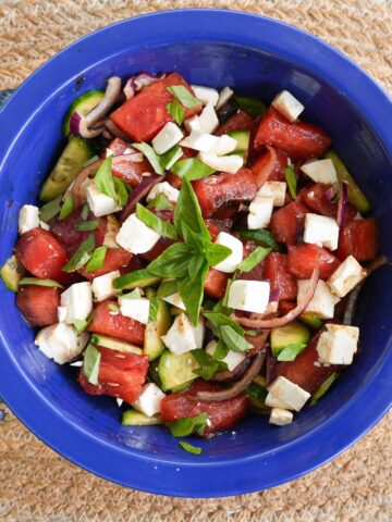 A bowl of watermelon salad topped with basil.