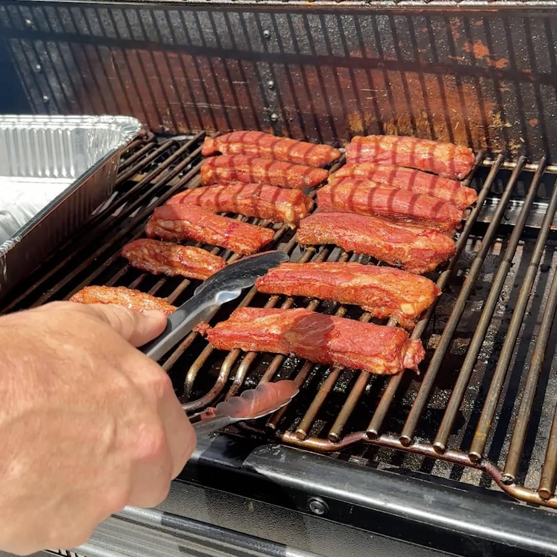 Ribs on smoker with a tong.