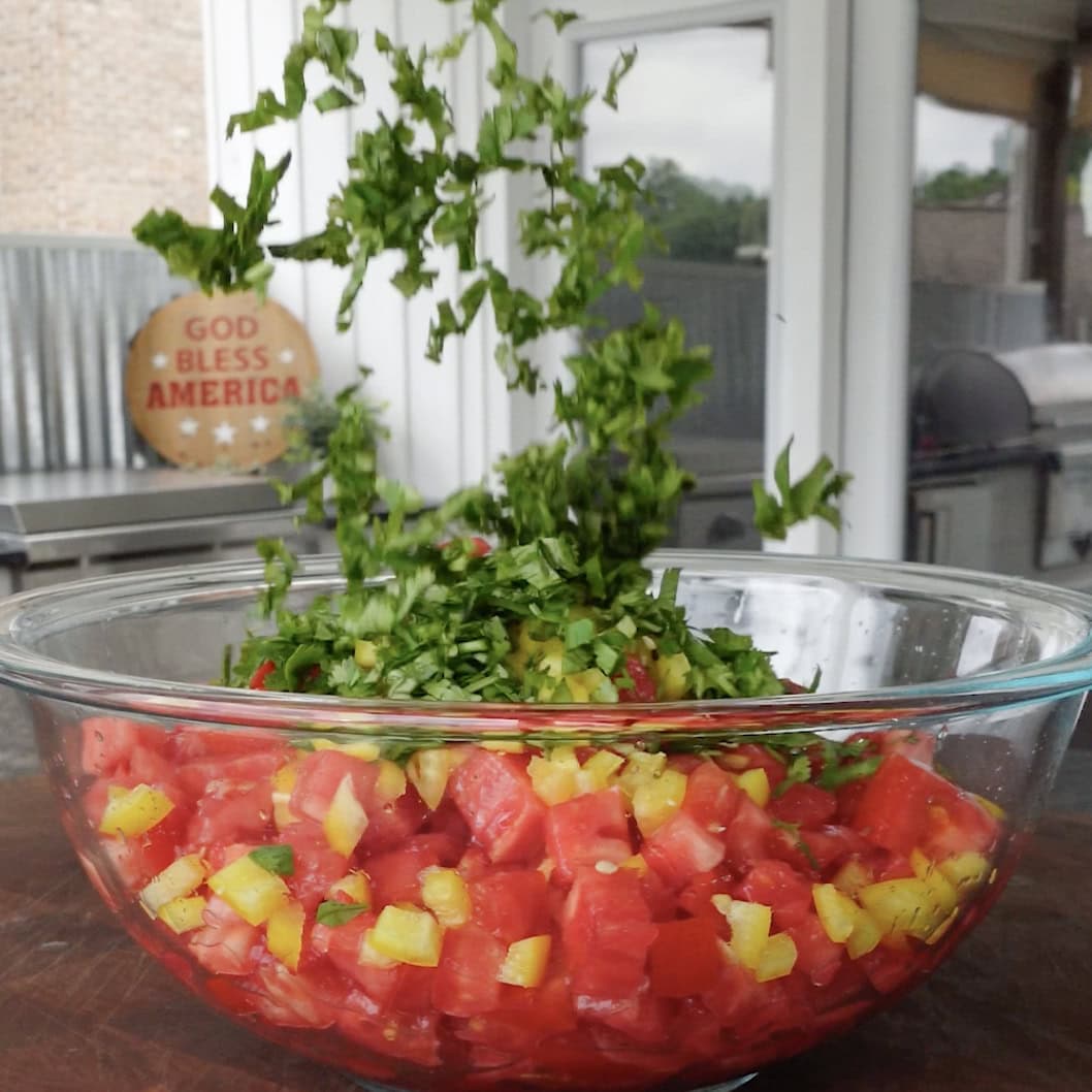 Cilantro going into a bowl of tomatoes.