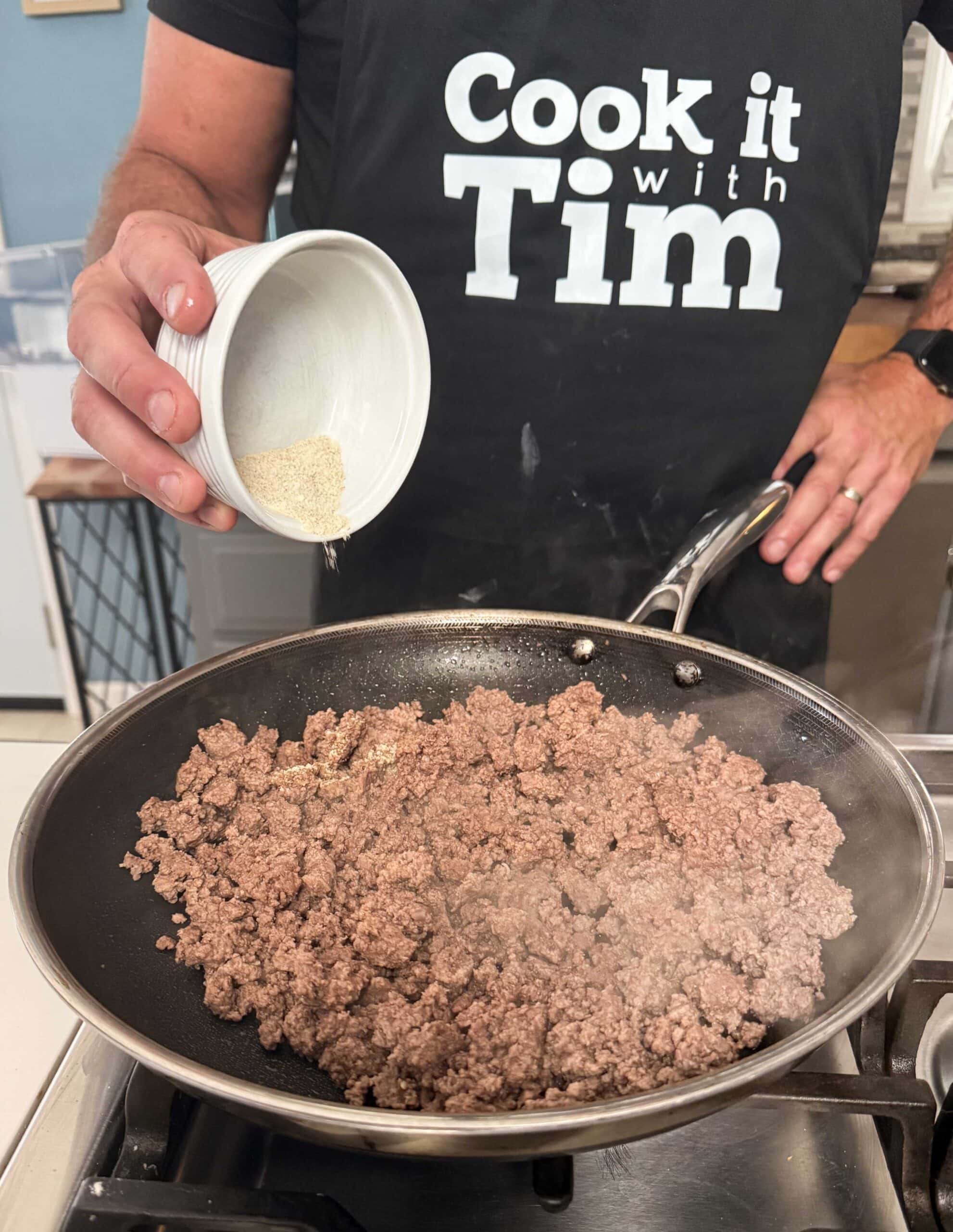Seasoning going into ground beef in a skillet.