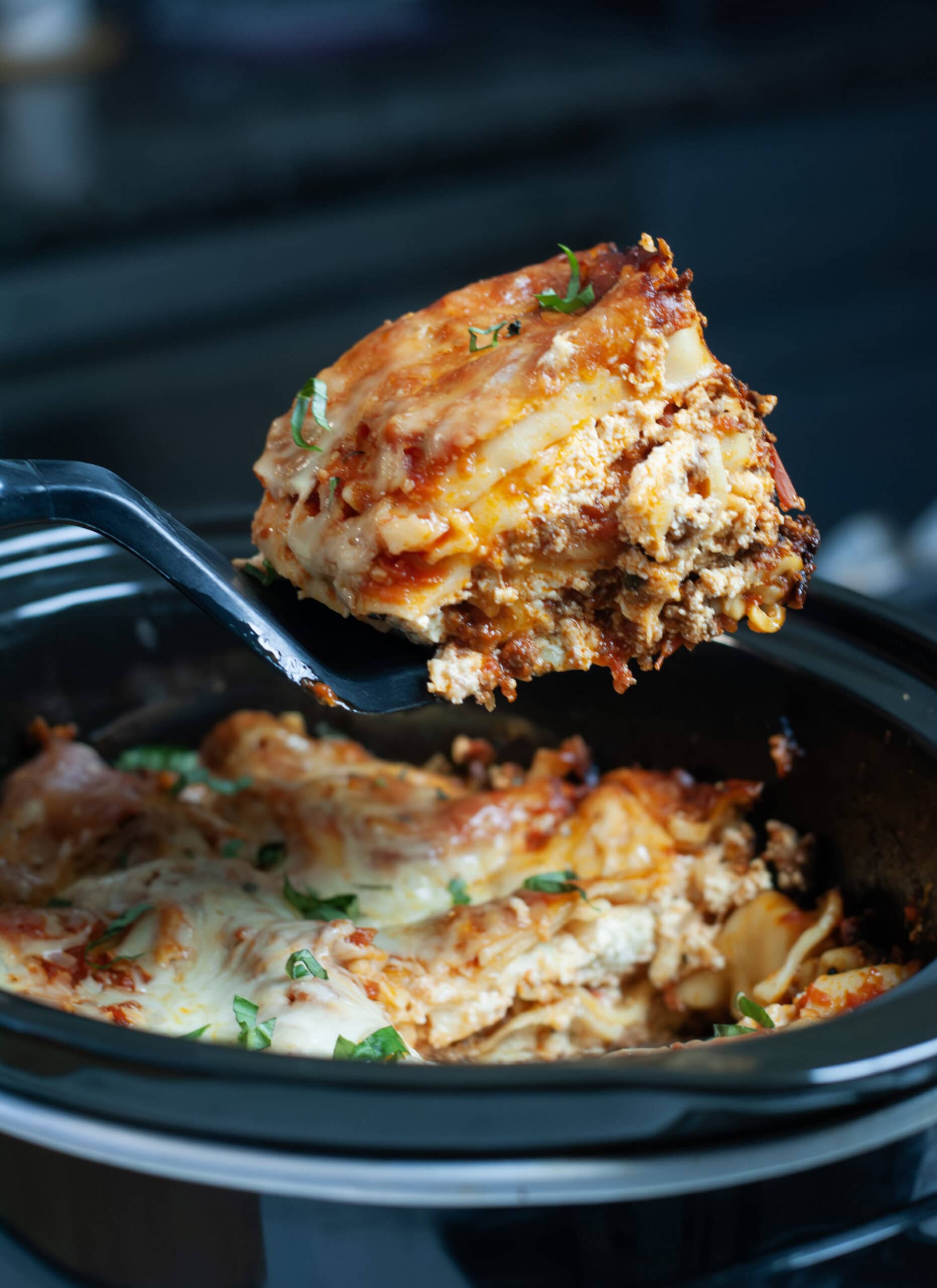 A scoop of lasagna with basil coming out of Slow Cooker.