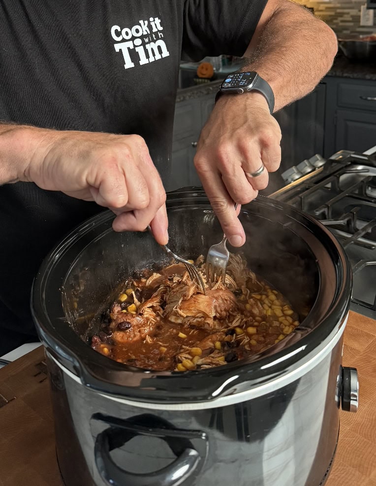 Chicken being shredded with forks.