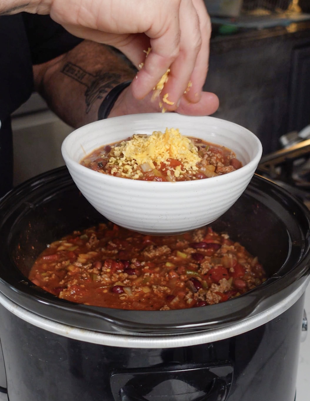 A bowl of chili with saltines, cheese and onions.