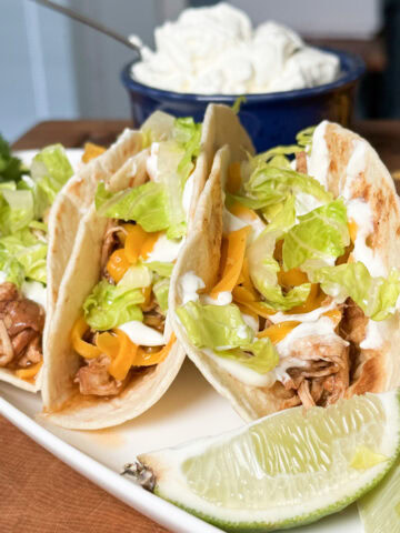Tacos with cheese and lettuce next to a lime wedge.