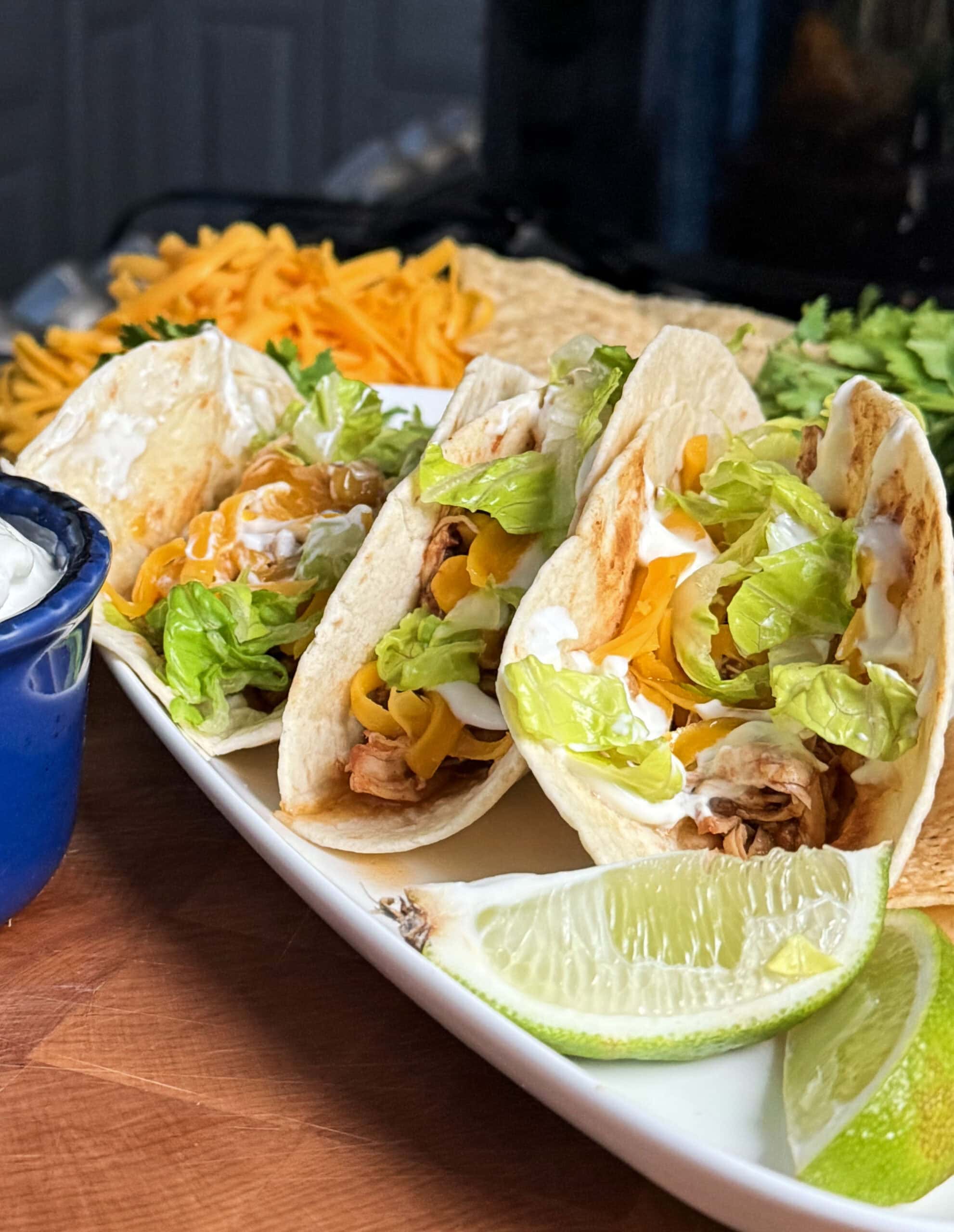 Tacos with cheese and lettuce next to a lime wedge.
