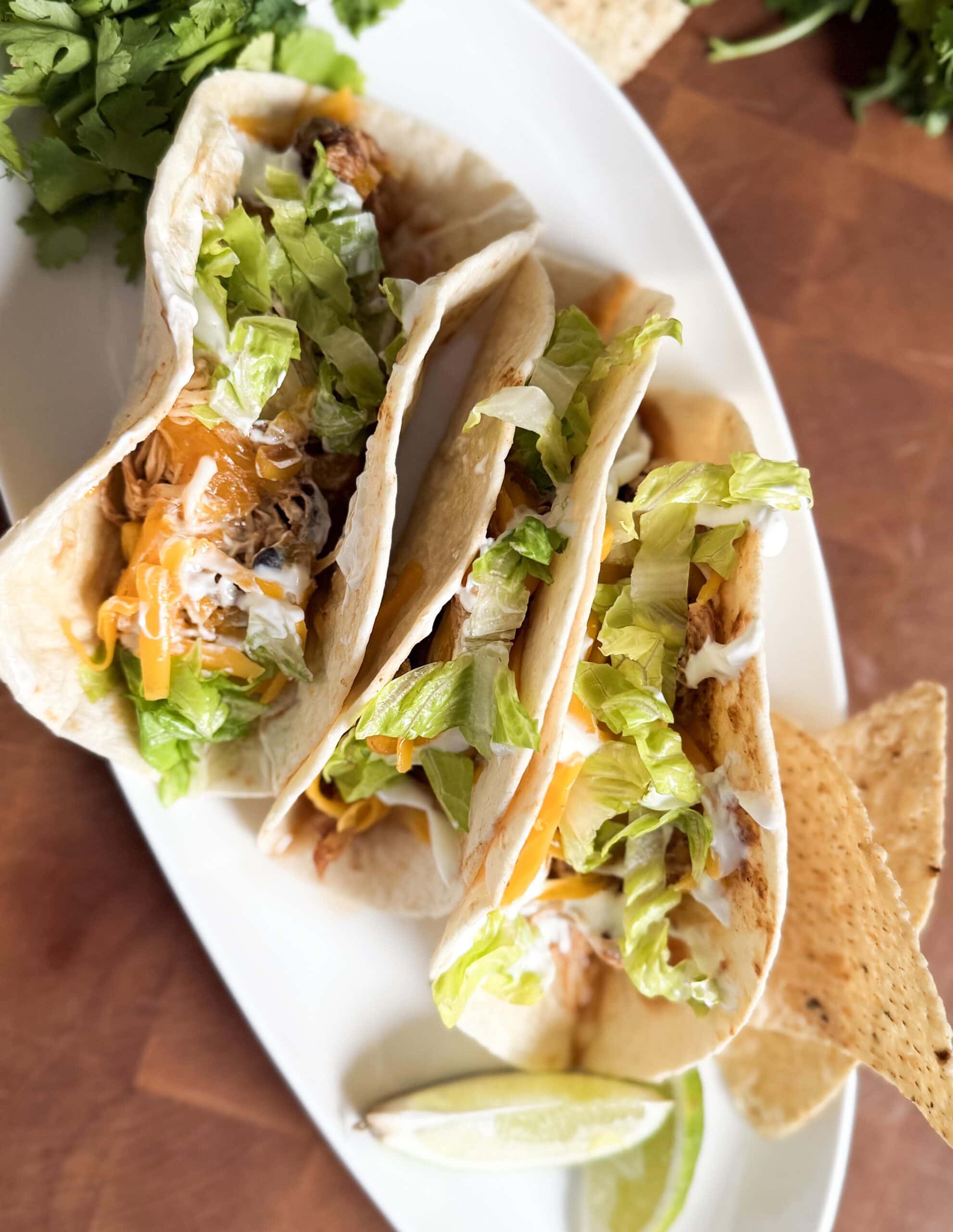 Tacos with cheese and lettuce next to a lime wedge.