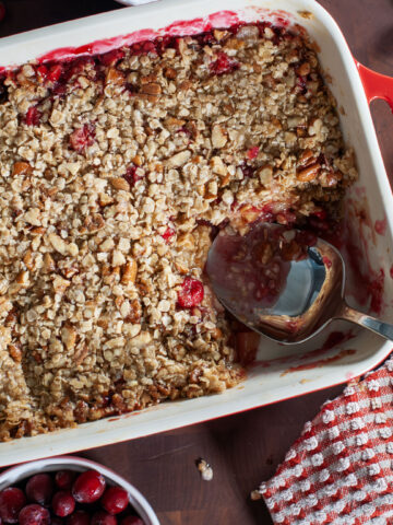 A large spoon in a baking dish full of cranberry apple crisp.