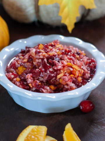 Cranberry relish in a white bowl next to orange slices.