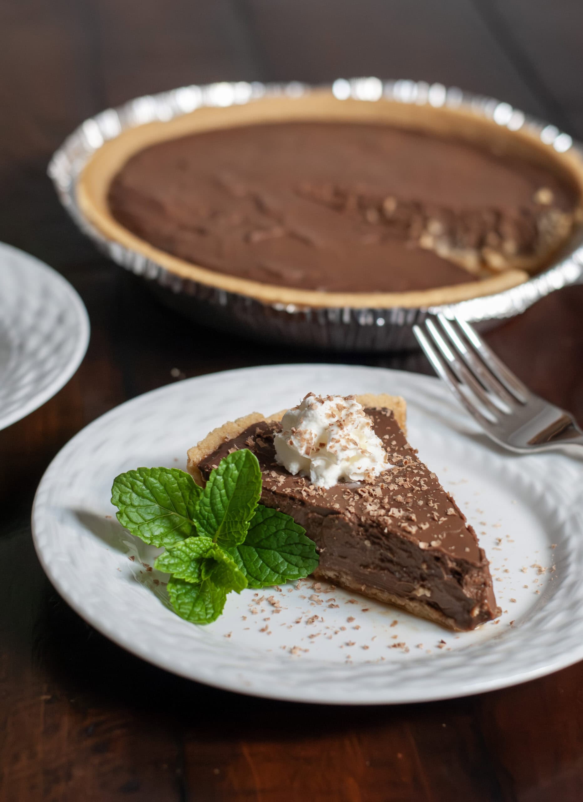 A slice of chocolate pie on a plate with whipped cream and mint leaves.
