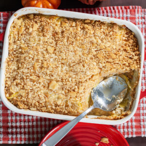 Squash casserole in a baking dish next to a serving of squash on a red plate.