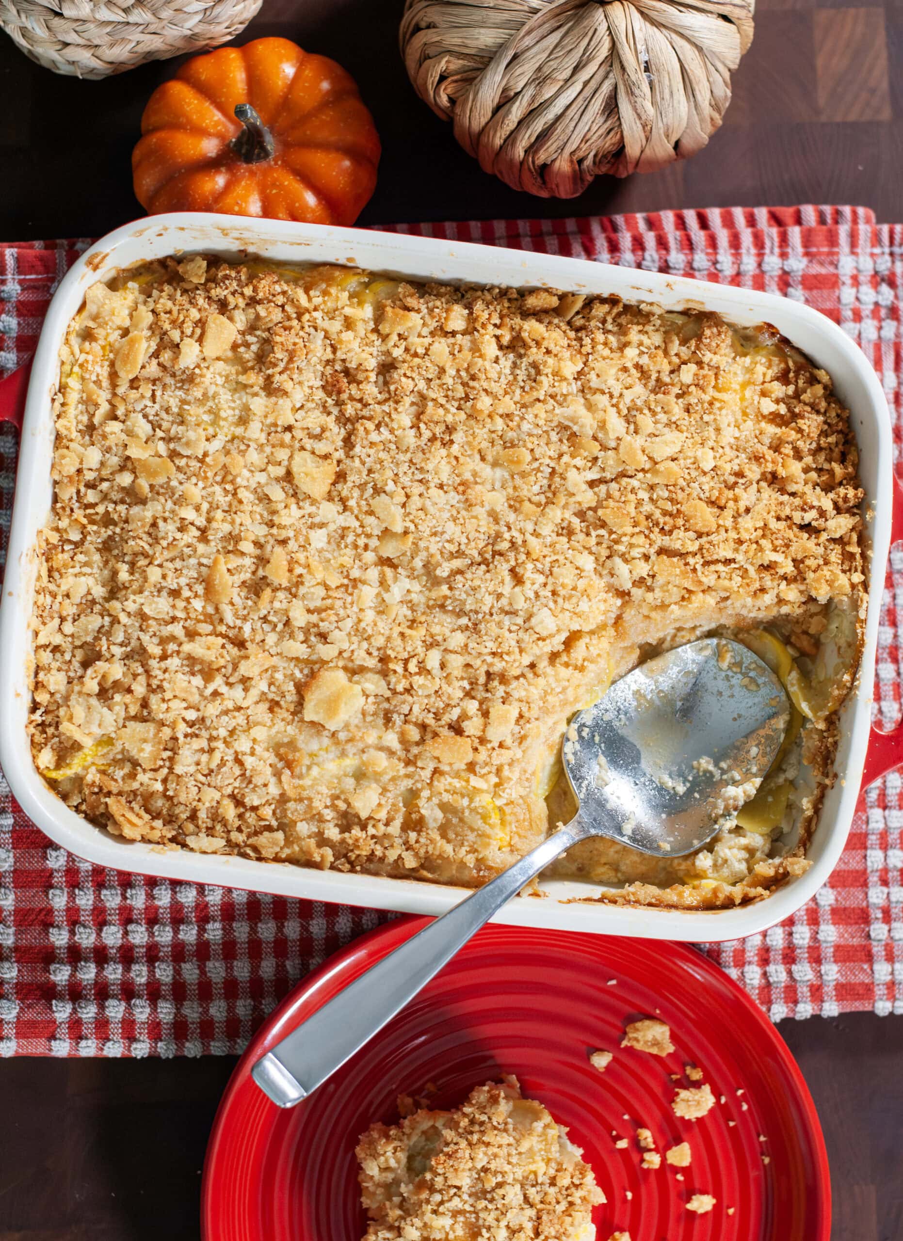 Squash casserole in a baking dish next to a serving of squash on a red plate.