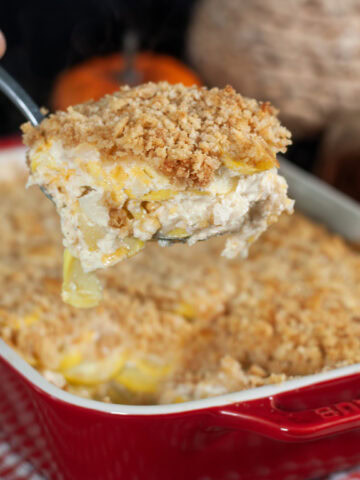 A scoop of squash casserole from a red baking dish.