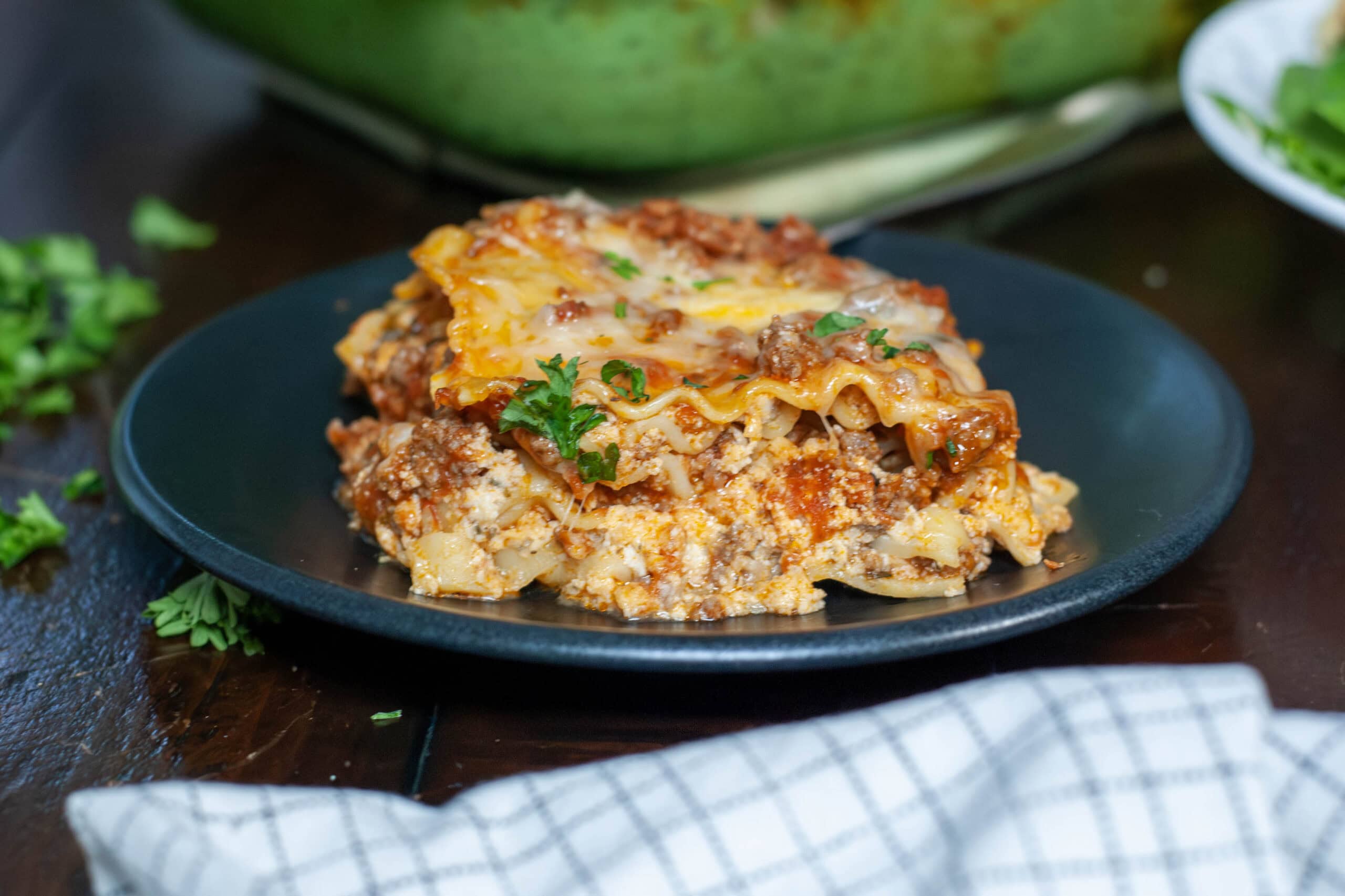 A slice of cottage cheese lasagna on a black plate with parsley.