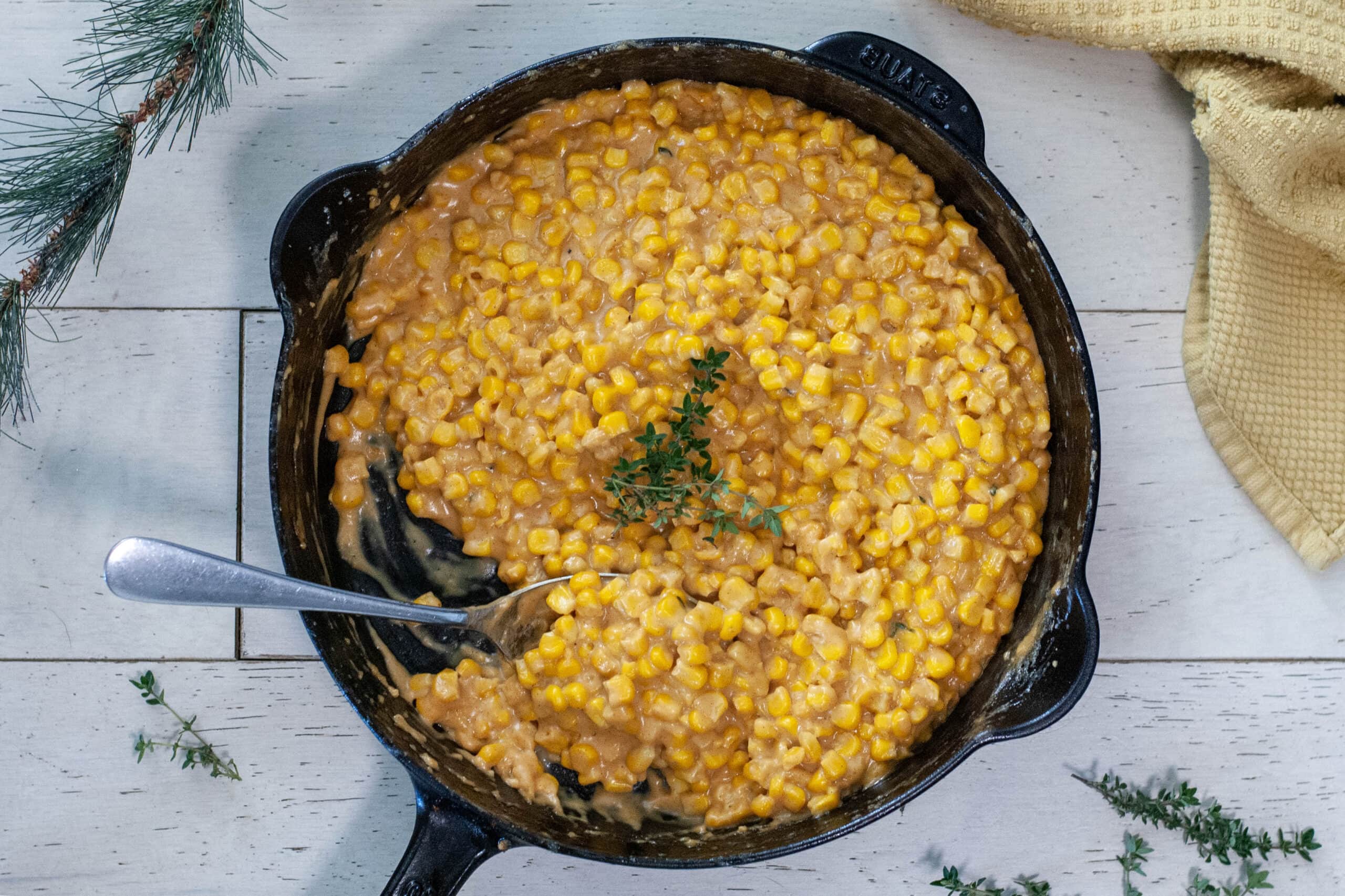 Creamy corn in a skillet with thyme sprigs.