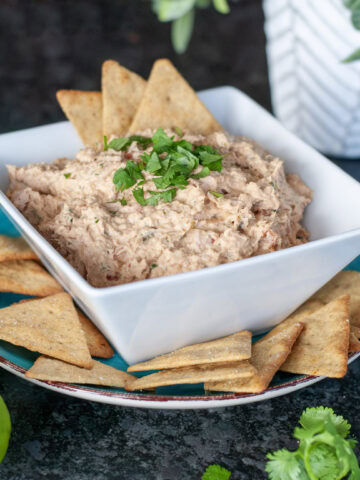 A bowl of Tuna Dip topped with cilantro next to limes and crackers.