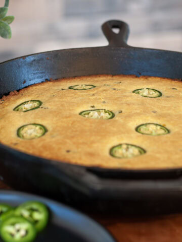 Smoked cornbread in a skillet next to sliced jalapeños.