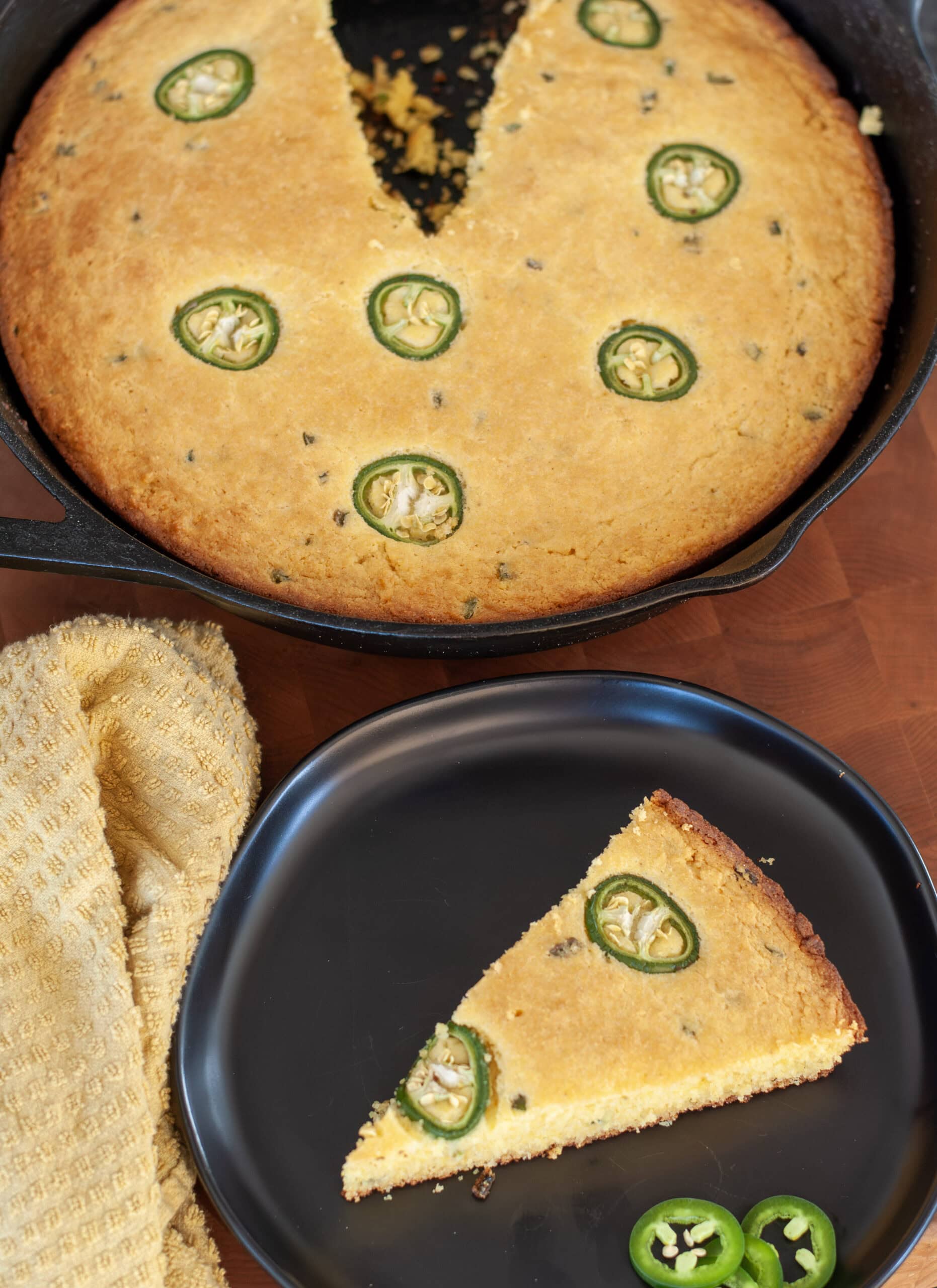 A slice of smoked cornbread on a black plate with jalapeños.
