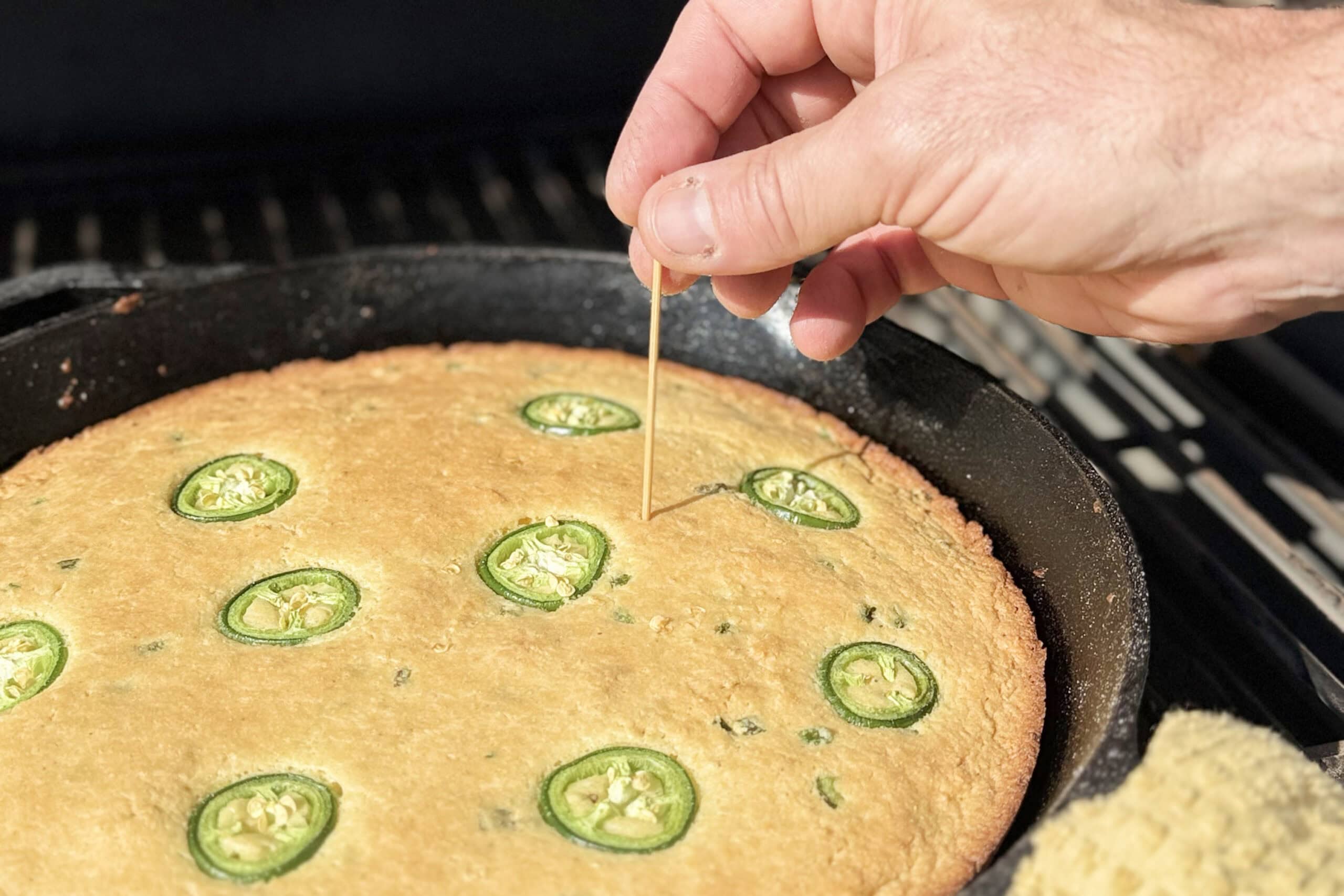 Toothpick going into smoked cornbread to check for doneness.