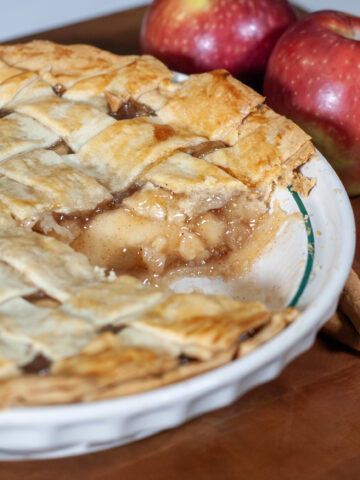 Apple pie in a dish next to cinnamon and apples.