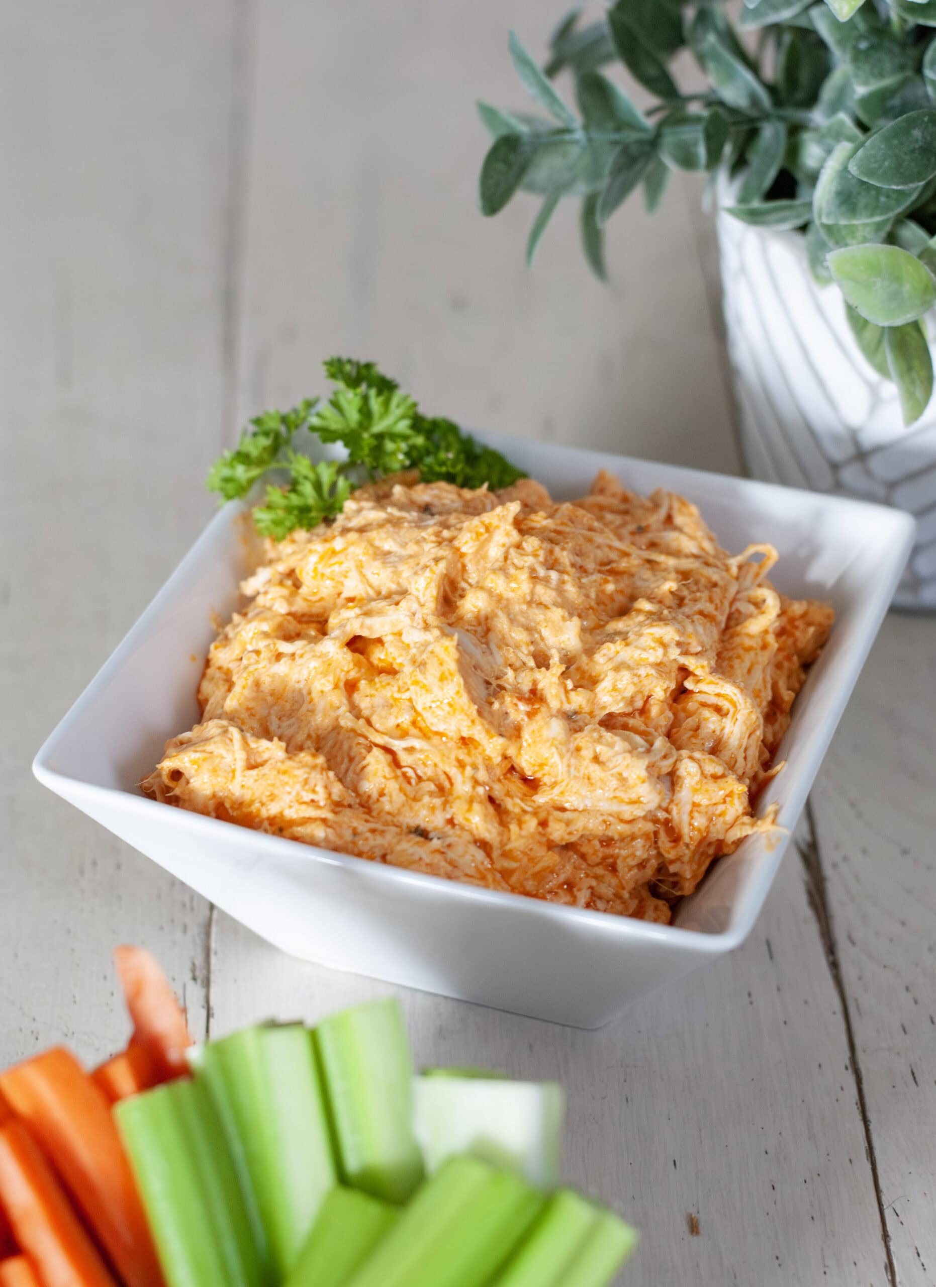A white bowl of buffalo chicken dip next to celery and carrots.