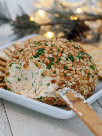 A cheese ball with a spreading knife and crackers.