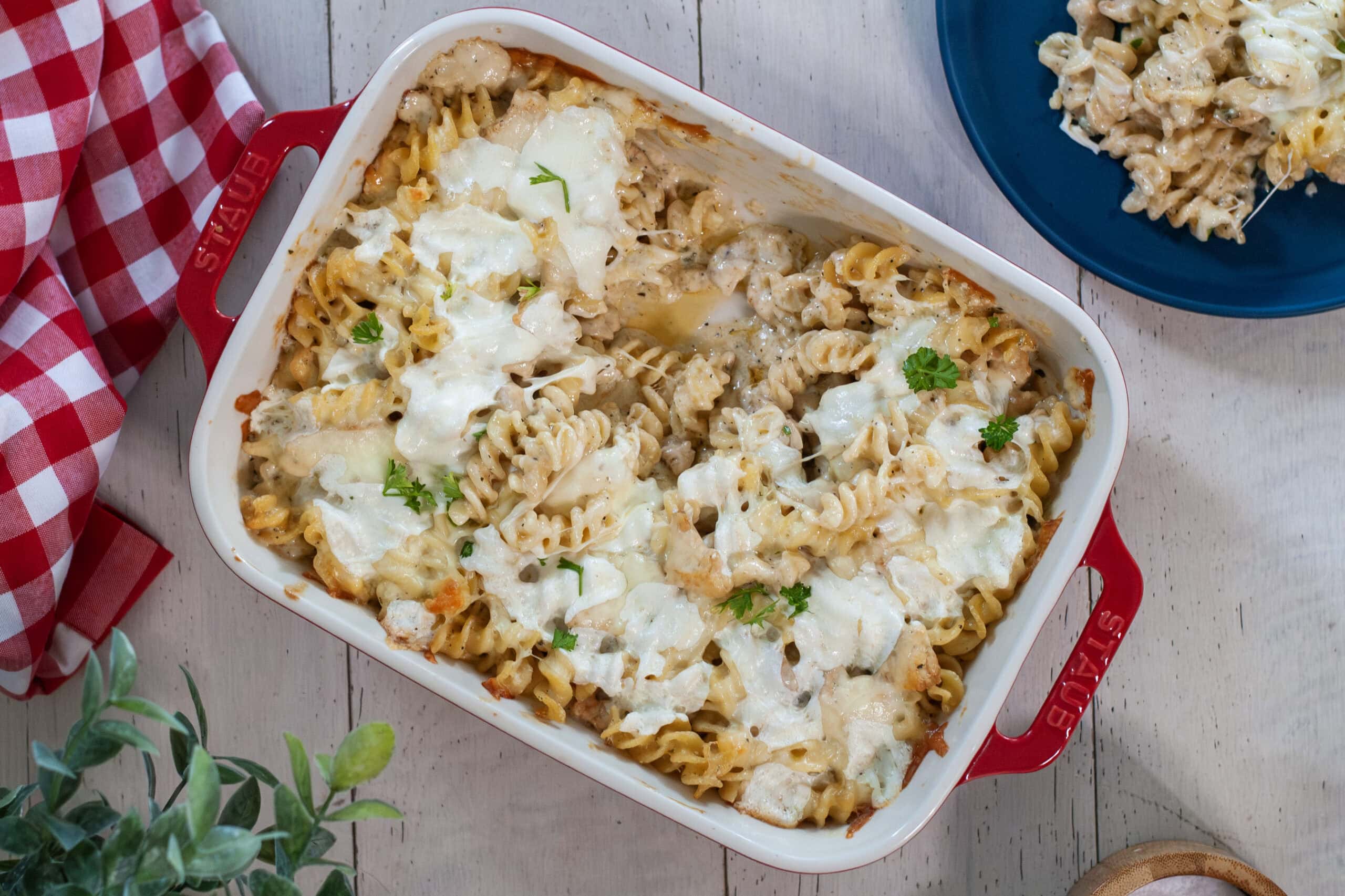 Chicken and pasta alfredo in a baking dish with parsley and red napkin.