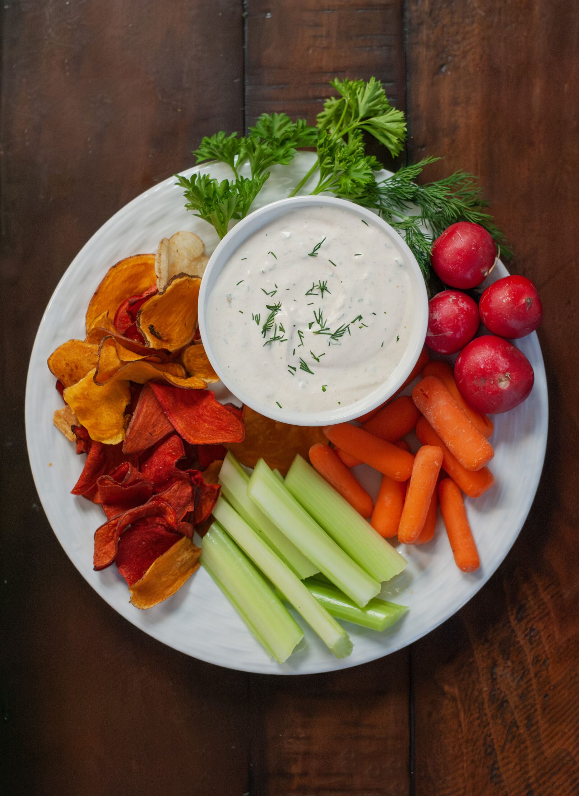 Dill dip on a plate with celery, carrots and chips.