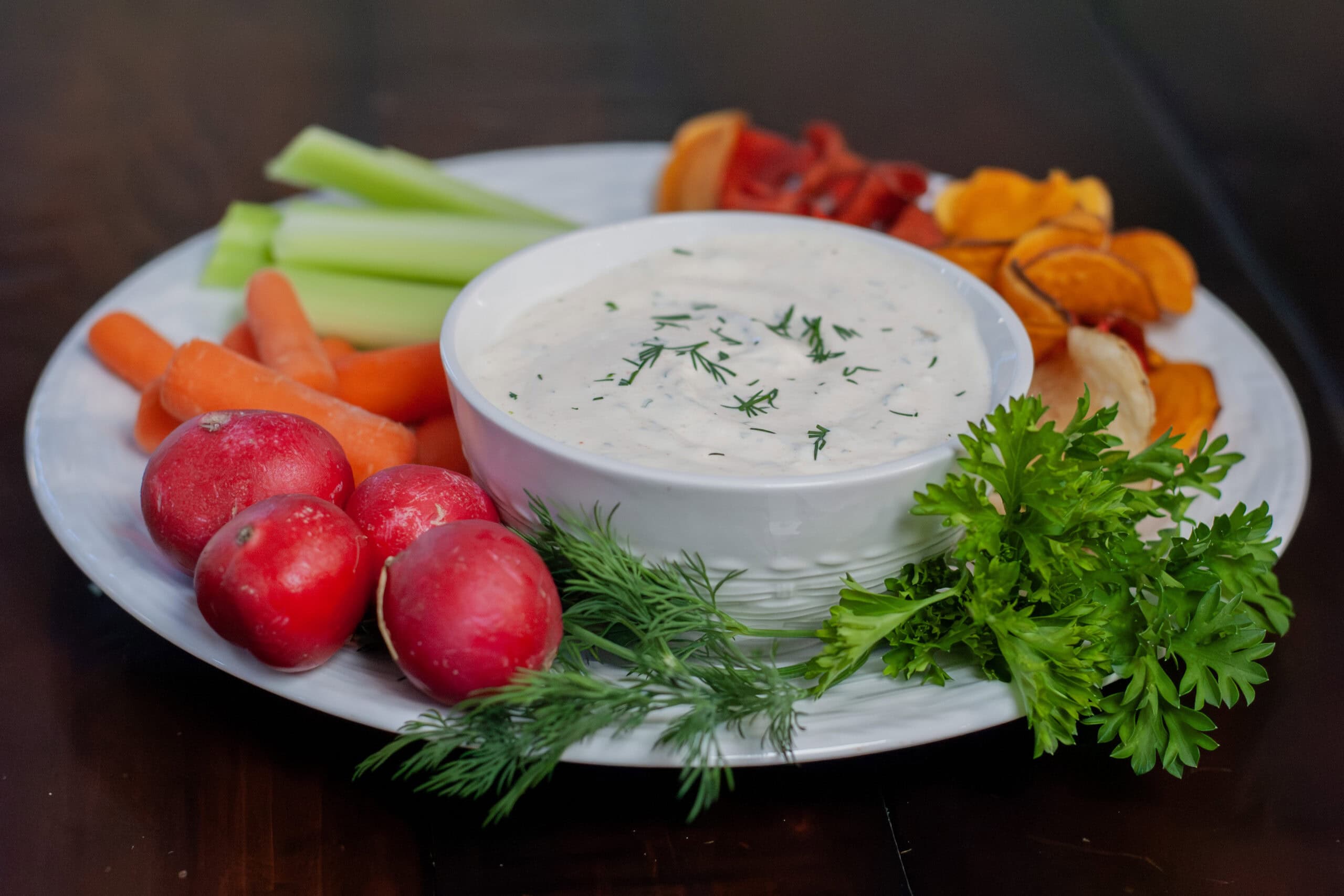A dip topped with dill on a plate with vegetables.