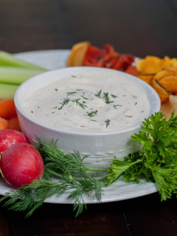 Dill dip on a plate with vegetables and fresh herbs.