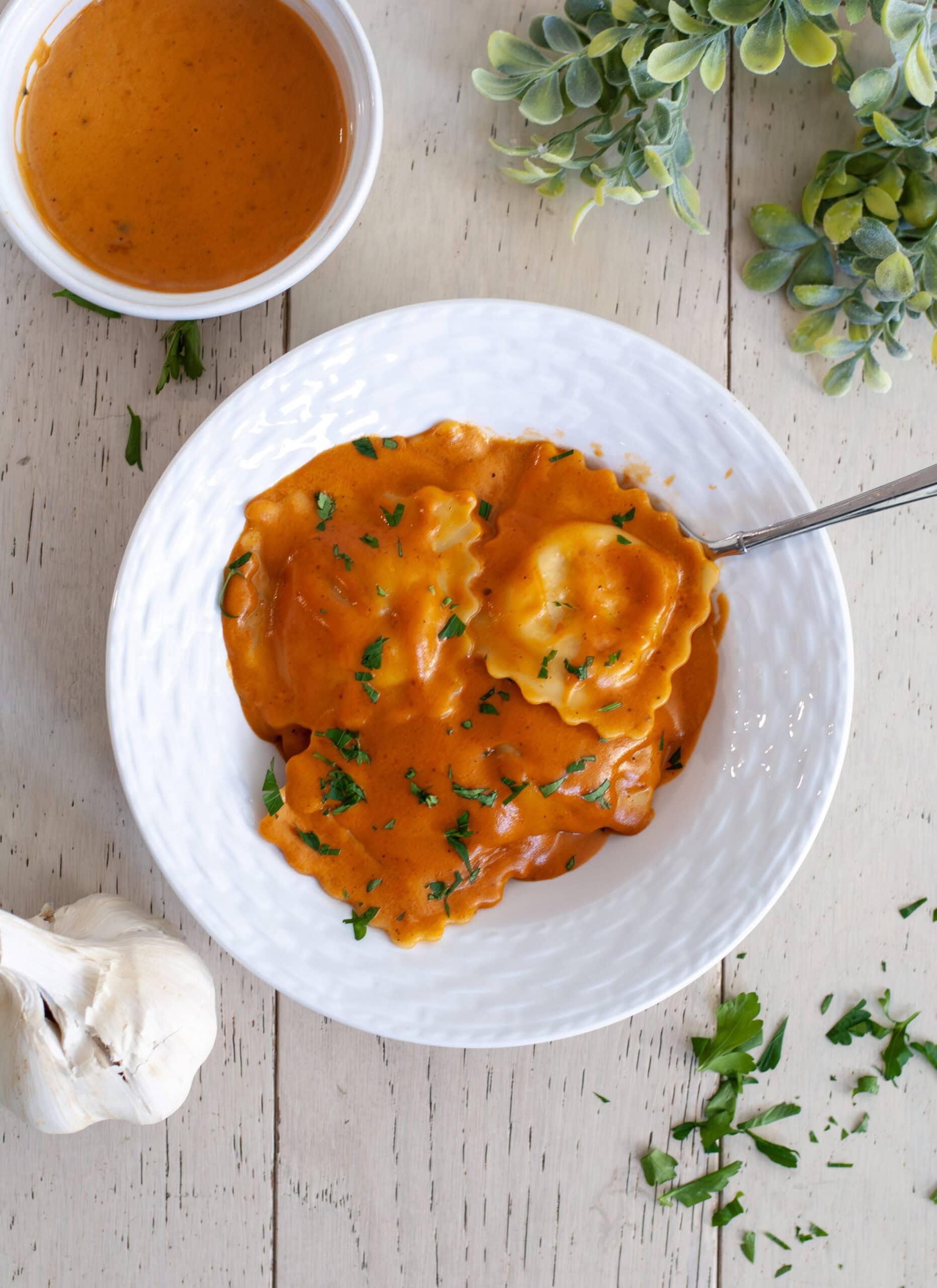 Lobster ravioli with sauce next to garlic cloves and parsley flakes.