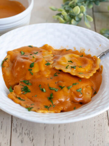 Sauce on ravioli in a white bowl topped with parsley.