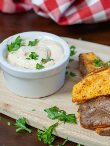 A dip with parsley next to sweet potato wedges.