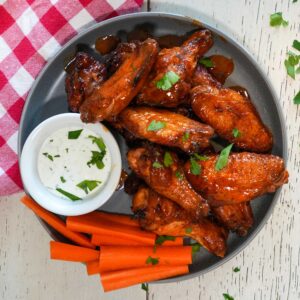 Chicken wings in buffalo sauce on a plate with carrots and ranch dressing.