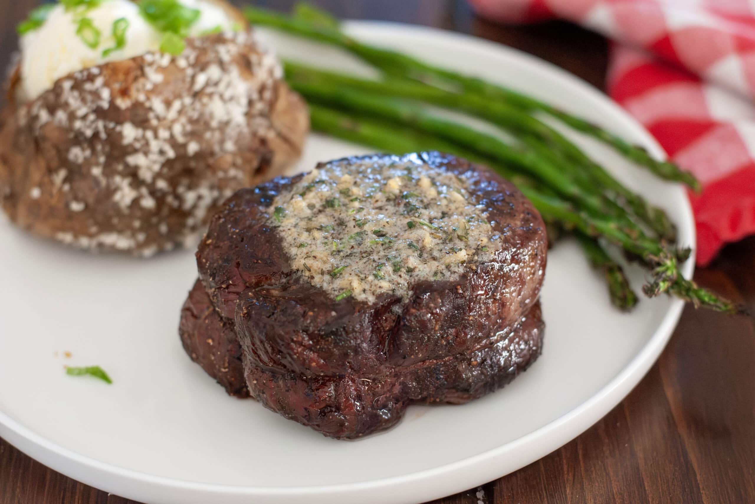 A grilled filet mignon with butter on a plate with vegetables.
