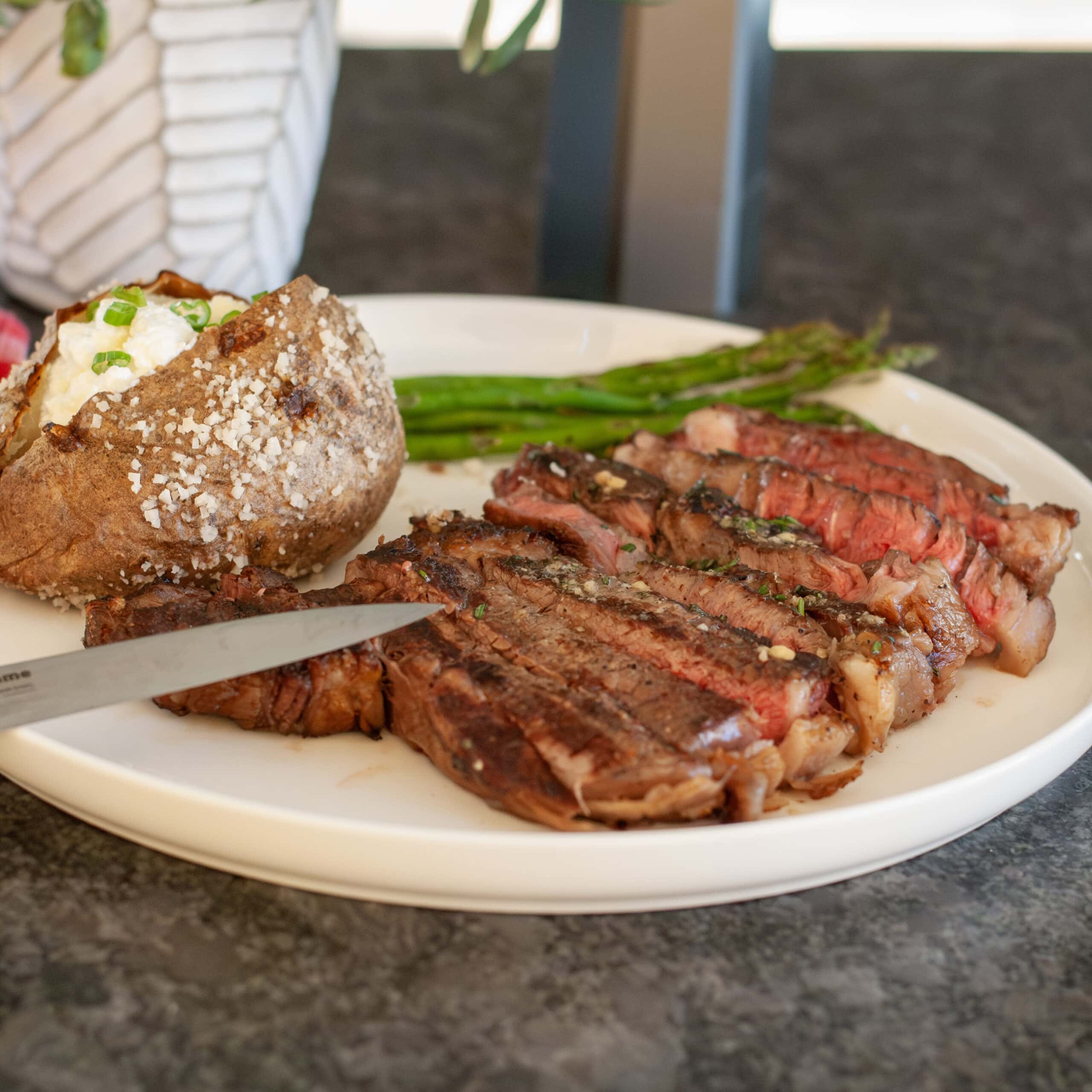 Grilled ribeye sliced on a plate with a potato.