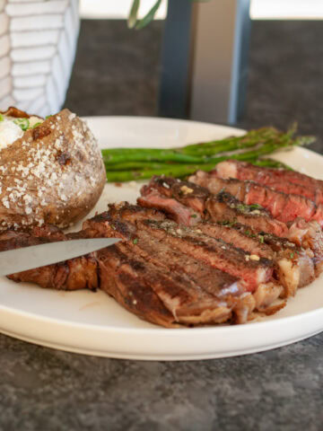 Slices of grilled ribeye on a plate with potatoes and asparagus.
