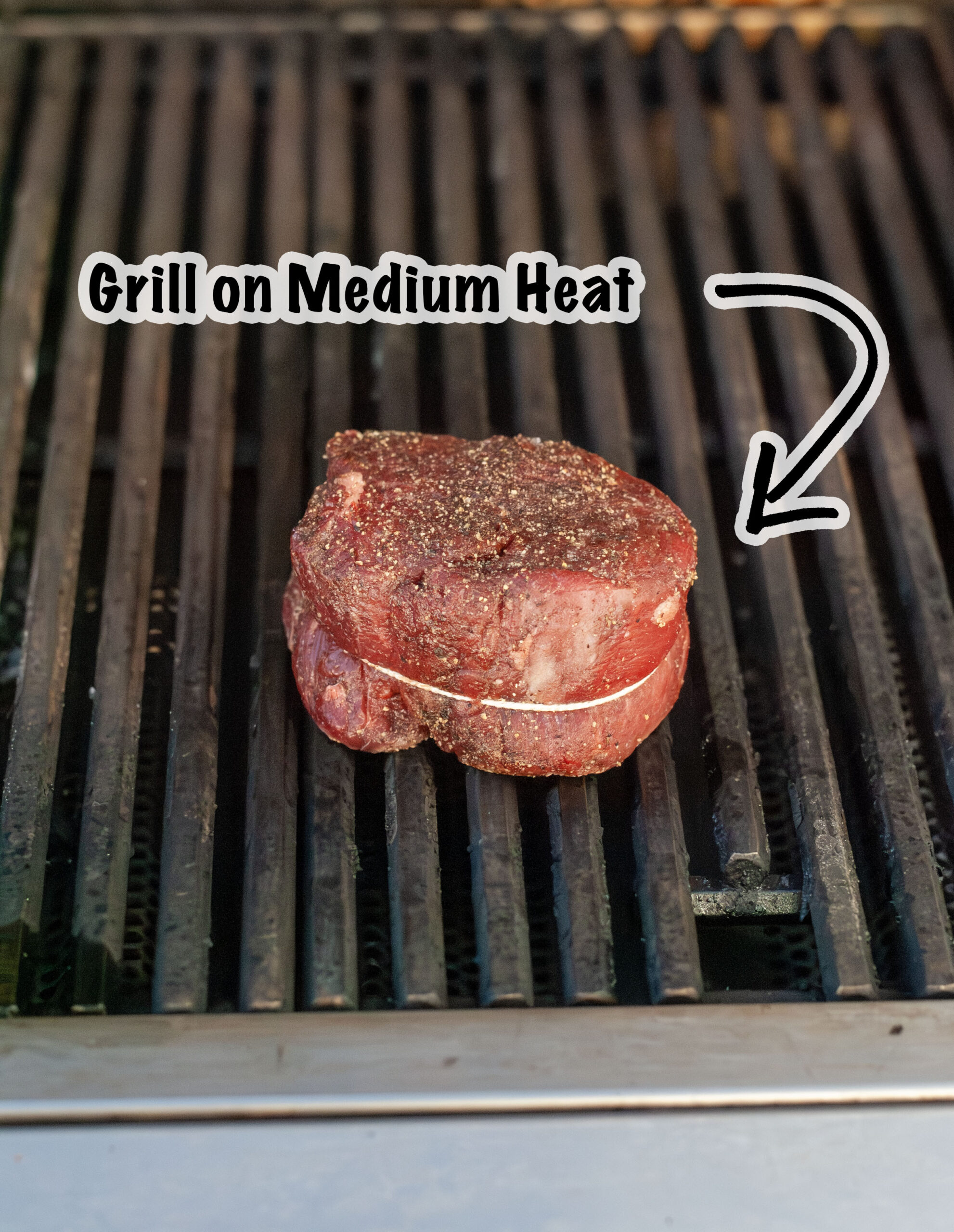 A filet mignon wrapped in twine grilling on medium heat on a grill.