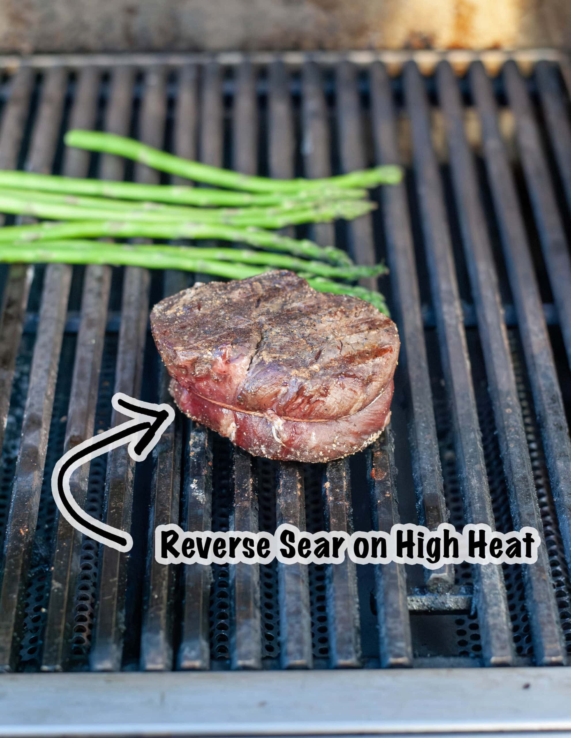 A steak reverse searing on a grill with asparagus.