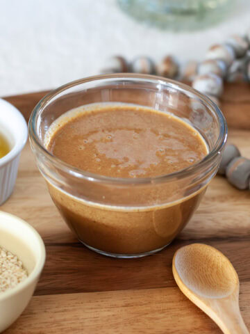 Tahini in a bowl next to sesame seeds and oil and a spoon.