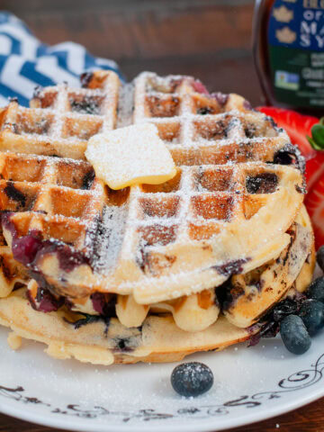 A blueberry waffle on a plate with blueberries and strawberries.
