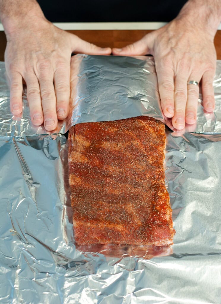 folding aluminum foil over a rack of ribs to cook in the oven.