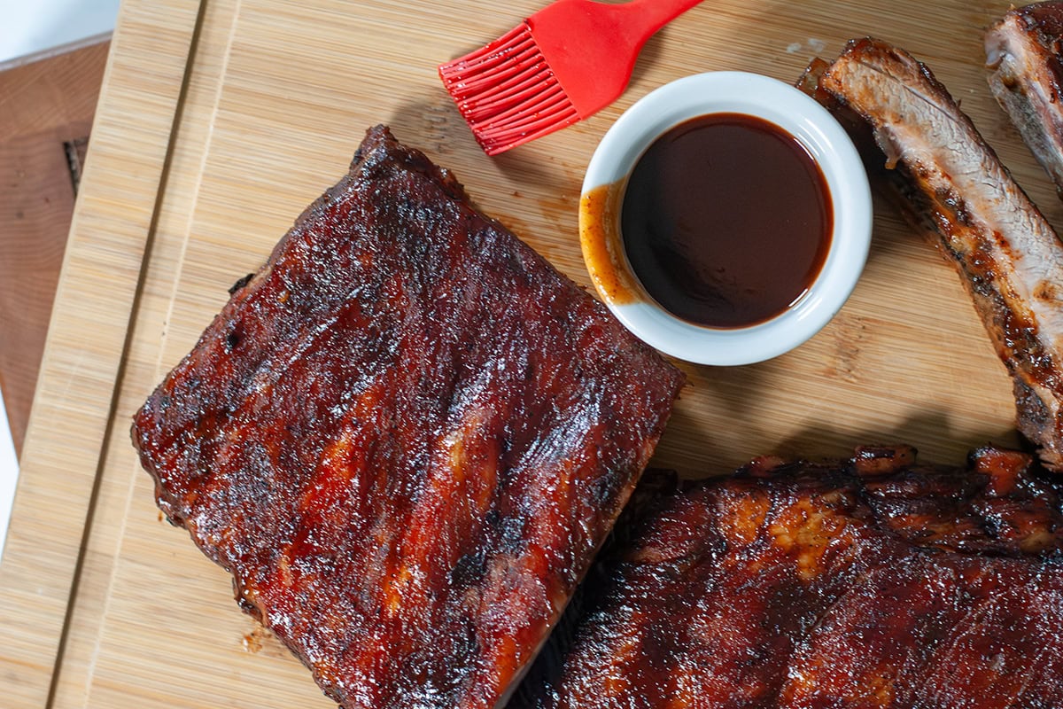 Ribs on a wooden board with sauce and a basting brush.
