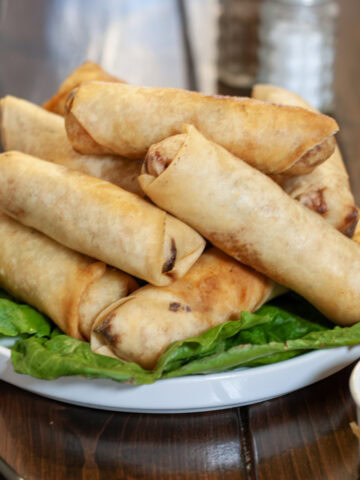 stack of golden brown egg rolls served on a white plate lined with lettuce leaves