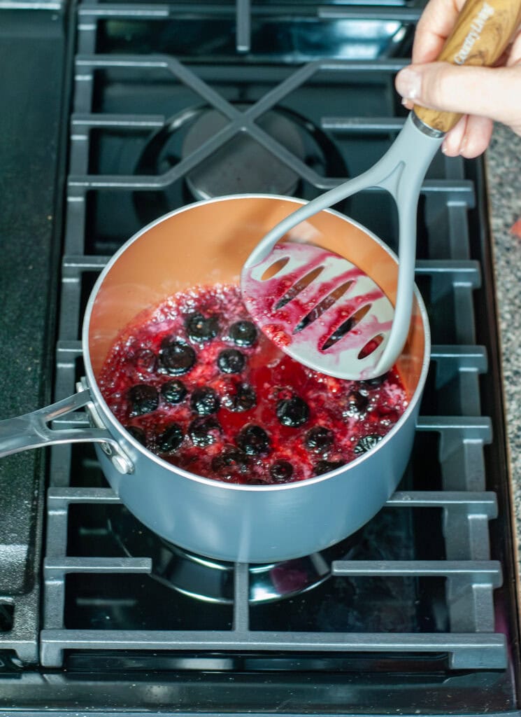 Blueberries being mashed in a pot.